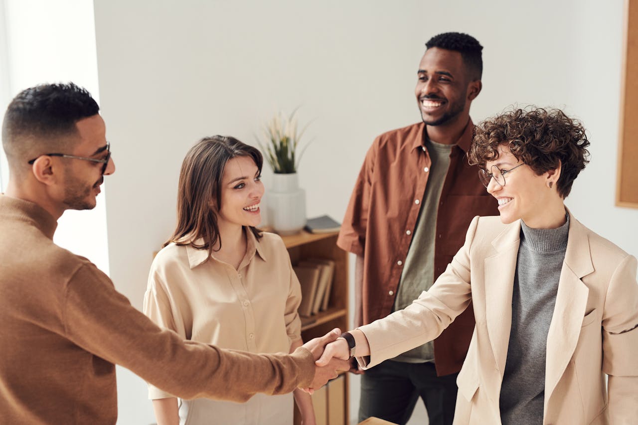 our-story Four colleagues smiling and shaking hands in a bright office setting.